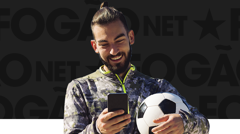 Imagem mostra homem sorrindo ao utilizar um celular e segurar uma bola de futebol