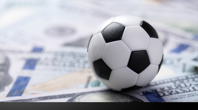 Imagem mostra uma bola de futebol em cima de notas de dinheiro